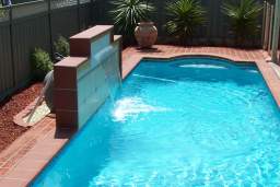 Concrete pool with a raised water feature wall and terracotta coping